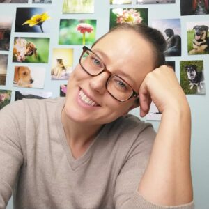 Selfie of Caitlin sitting in front of a wall covered in 4x6 photo prints.